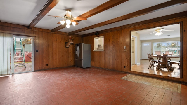 living room with brick floor, wooden walls, a ceiling fan, and beamed ceiling