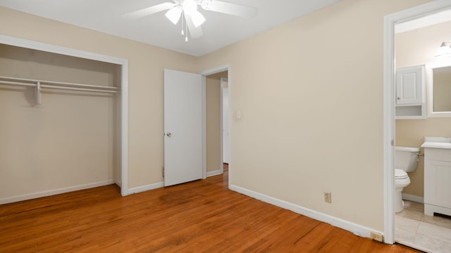 unfurnished bedroom with baseboards, a ceiling fan, ensuite bath, light wood-type flooring, and a closet