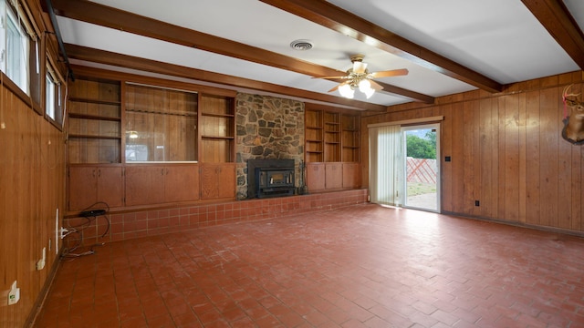 unfurnished living room featuring brick floor, wooden walls, a ceiling fan, visible vents, and beam ceiling