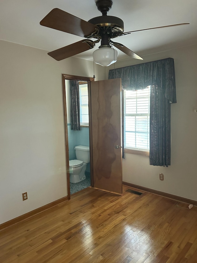 unfurnished bedroom featuring multiple windows, hardwood / wood-style floors, and ensuite bathroom