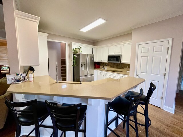 kitchen with a kitchen bar, kitchen peninsula, stainless steel appliances, white cabinets, and light hardwood / wood-style floors