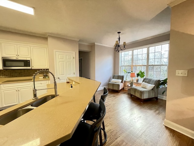 kitchen featuring white cabinetry, sink, a notable chandelier, pendant lighting, and ornamental molding