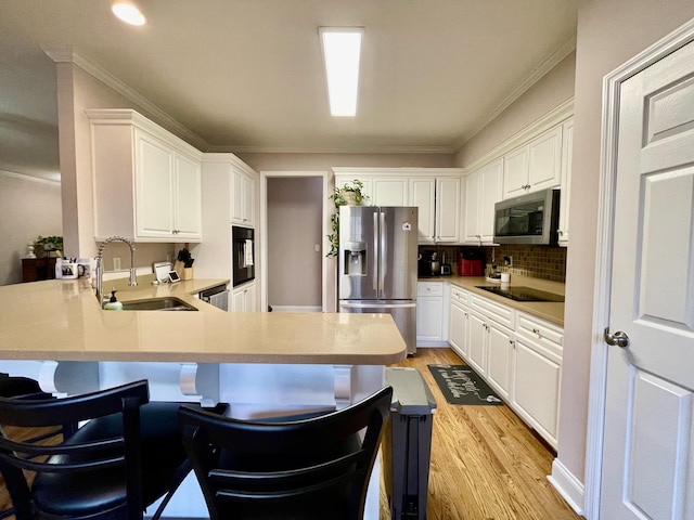 kitchen with sink, kitchen peninsula, a breakfast bar area, white cabinets, and black appliances