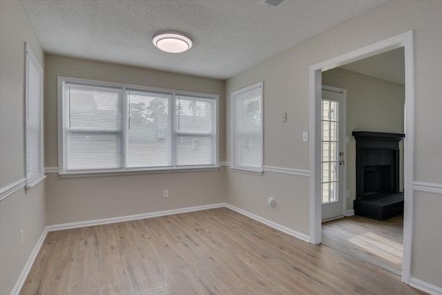 spare room featuring light wood-style flooring, a textured ceiling, baseboards, and a fireplace with raised hearth