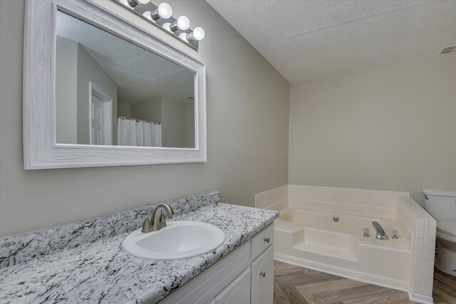 bathroom featuring toilet, a textured ceiling, vanity, and a bath