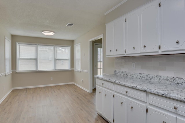 kitchen with white cabinetry, visible vents, baseboards, and light wood-type flooring