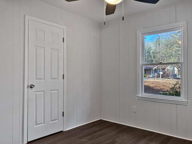 spare room featuring wood walls, ceiling fan, a healthy amount of sunlight, and dark hardwood / wood-style flooring