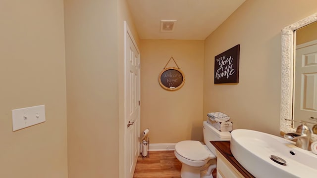 half bathroom featuring visible vents, toilet, wood finished floors, baseboards, and vanity