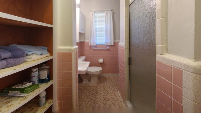 bathroom featuring a shower with shower door, tile walls, and toilet