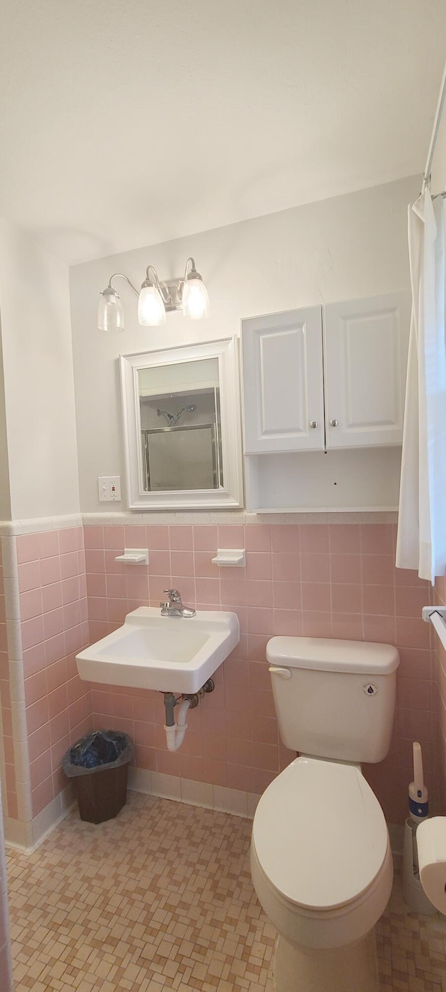 bathroom with toilet, sink, and tile walls