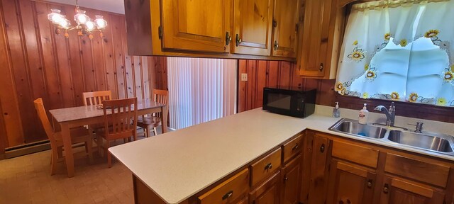 kitchen featuring sink, an inviting chandelier, kitchen peninsula, wood walls, and pendant lighting