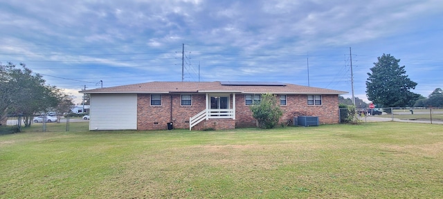 rear view of house with solar panels, cooling unit, and a yard