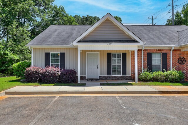 view of front of home featuring a shingled roof, a porch, uncovered parking, and brick siding