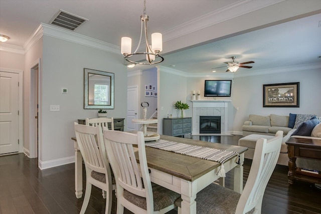 dining room with a fireplace, dark wood-type flooring, ceiling fan with notable chandelier, and ornamental molding