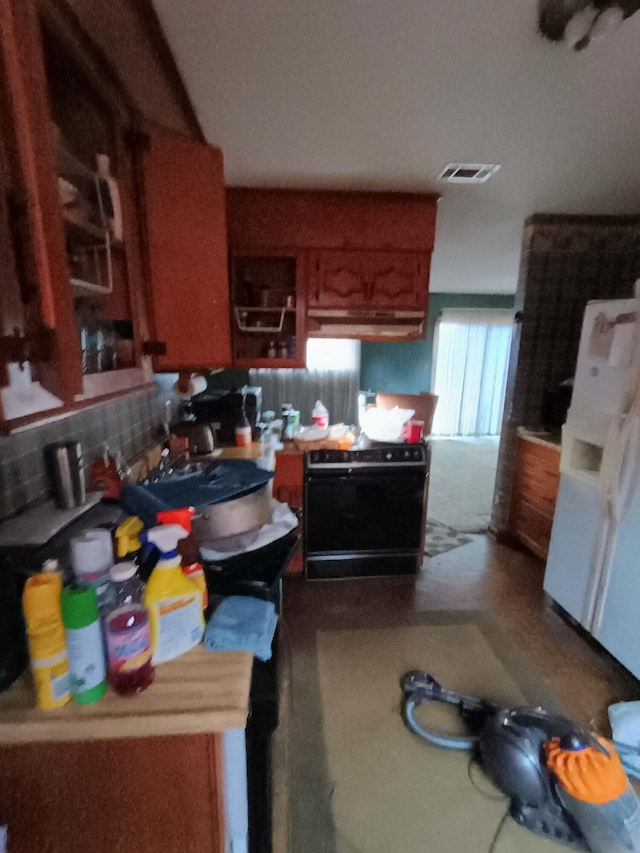 kitchen featuring visible vents, backsplash, brown cabinetry, freestanding refrigerator, and black range