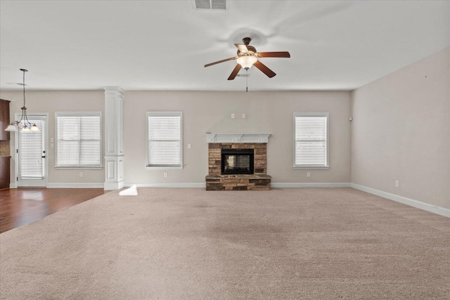 unfurnished living room with ceiling fan, a wealth of natural light, dark carpet, and a stone fireplace