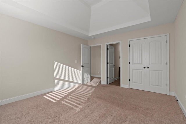 unfurnished bedroom with light carpet, a closet, and a raised ceiling