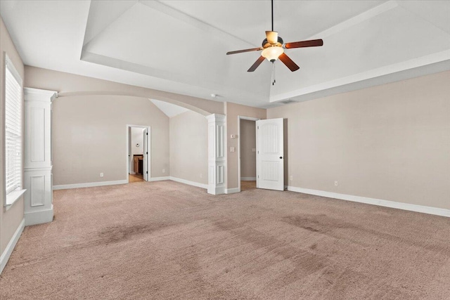 carpeted empty room featuring ceiling fan, a raised ceiling, ornate columns, and vaulted ceiling