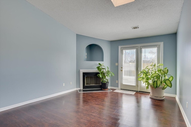 unfurnished living room with wood finished floors, a glass covered fireplace, visible vents, and baseboards