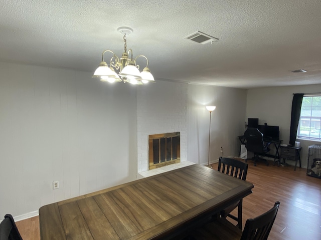 3406 Pine Hill Rd, Hephzibah, GA 30815 - dining room featuring a textured ceiling, visible vents, a brick fireplace, wood finished floors, and a chandelier