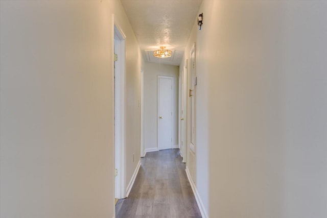 corridor with attic access, a textured ceiling, baseboards, and wood finished floors