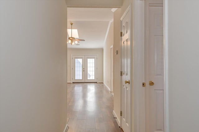 hall with light wood finished floors, baseboards, ornamental molding, and french doors