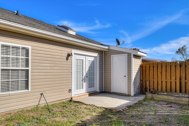 property entrance with a patio, french doors, roof with shingles, and fence