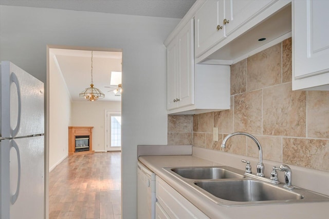 kitchen featuring light countertops, a glass covered fireplace, white cabinetry, a sink, and white appliances