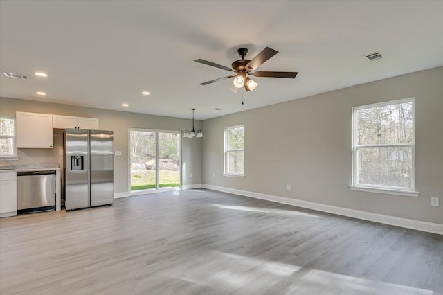 unfurnished living room featuring ceiling fan with notable chandelier, light hardwood / wood-style floors, and a wealth of natural light