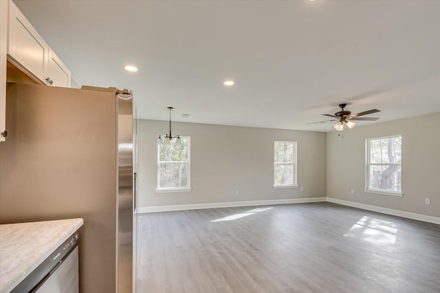 kitchen featuring stainless steel fridge, ceiling fan with notable chandelier, a healthy amount of sunlight, pendant lighting, and white cabinetry