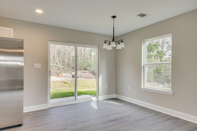 unfurnished dining area with wood-type flooring, an inviting chandelier, and a wealth of natural light