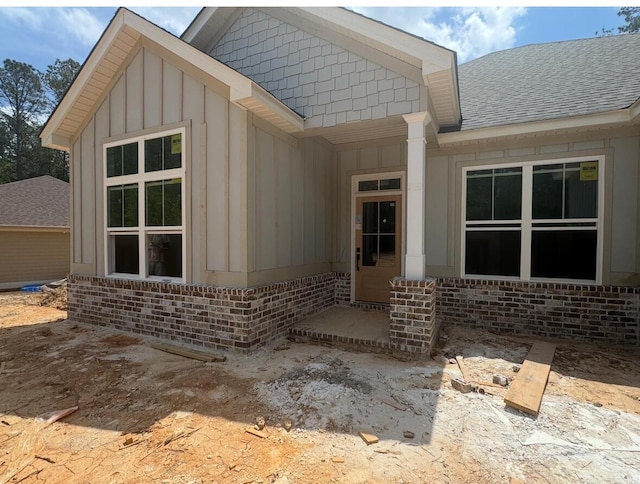 doorway to property with board and batten siding, a shingled roof, and brick siding