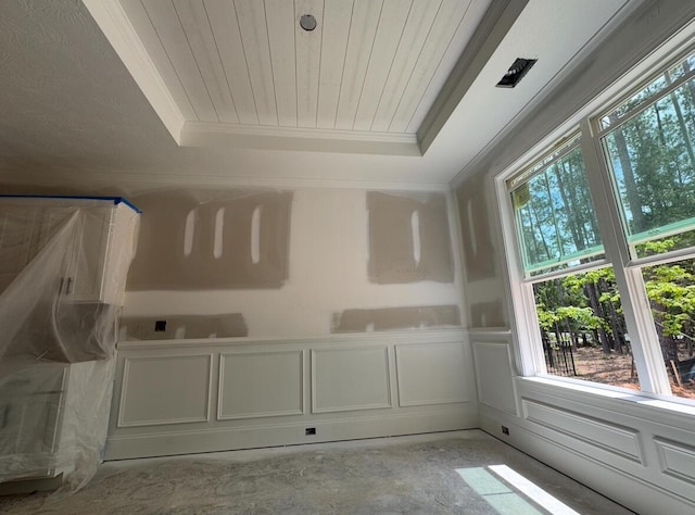 spare room featuring wooden ceiling, concrete floors, a raised ceiling, and ornamental molding