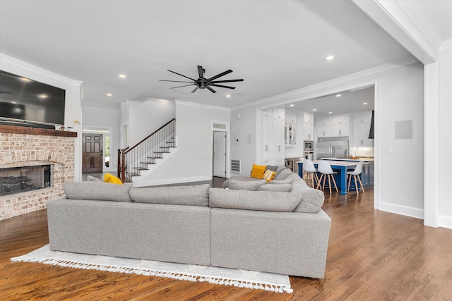 living room with a brick fireplace, ceiling fan, dark hardwood / wood-style floors, and ornamental molding