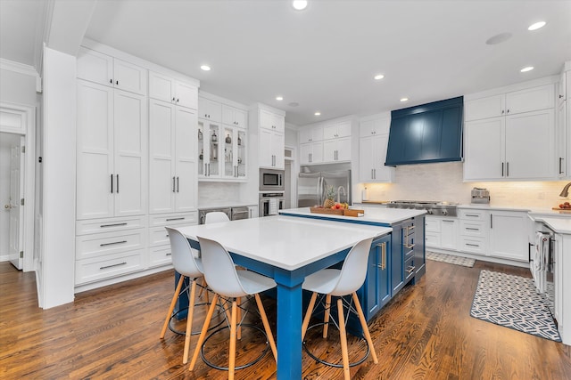 kitchen featuring a kitchen bar, blue cabinetry, built in appliances, white cabinets, and a kitchen island