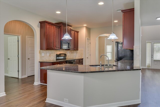 kitchen with dark wood finished floors, arched walkways, freestanding refrigerator, a sink, and black range with electric stovetop