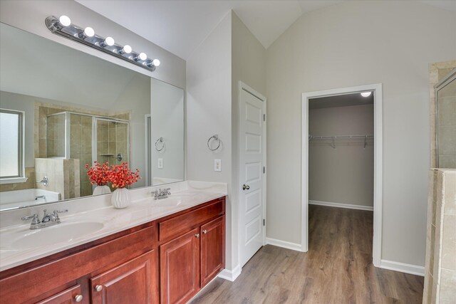 full bathroom with wood finished floors, double vanity, a sink, a spacious closet, and a stall shower