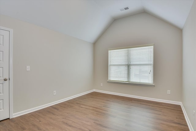 empty room with lofted ceiling, wood finished floors, visible vents, and baseboards