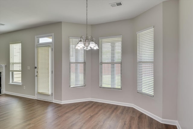 unfurnished dining area with visible vents, a healthy amount of sunlight, a chandelier, baseboards, and dark wood-type flooring