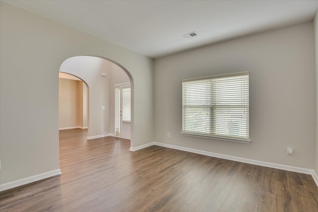 empty room with dark wood-style floors, arched walkways, visible vents, and baseboards