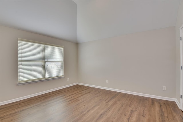 spare room featuring baseboards, wood finished floors, and vaulted ceiling