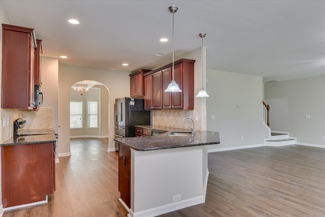 kitchen with dark stone counters, a sink, backsplash, arched walkways, and wood finished floors