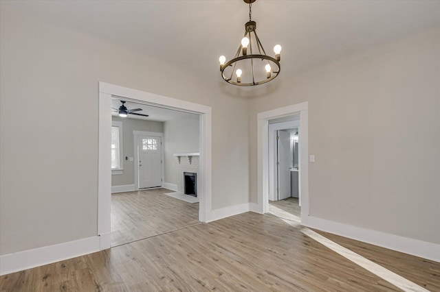 unfurnished dining area featuring a brick fireplace, ceiling fan with notable chandelier, and light wood-type flooring