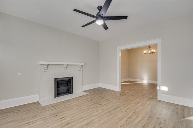 unfurnished living room with a brick fireplace, ceiling fan with notable chandelier, and light hardwood / wood-style flooring