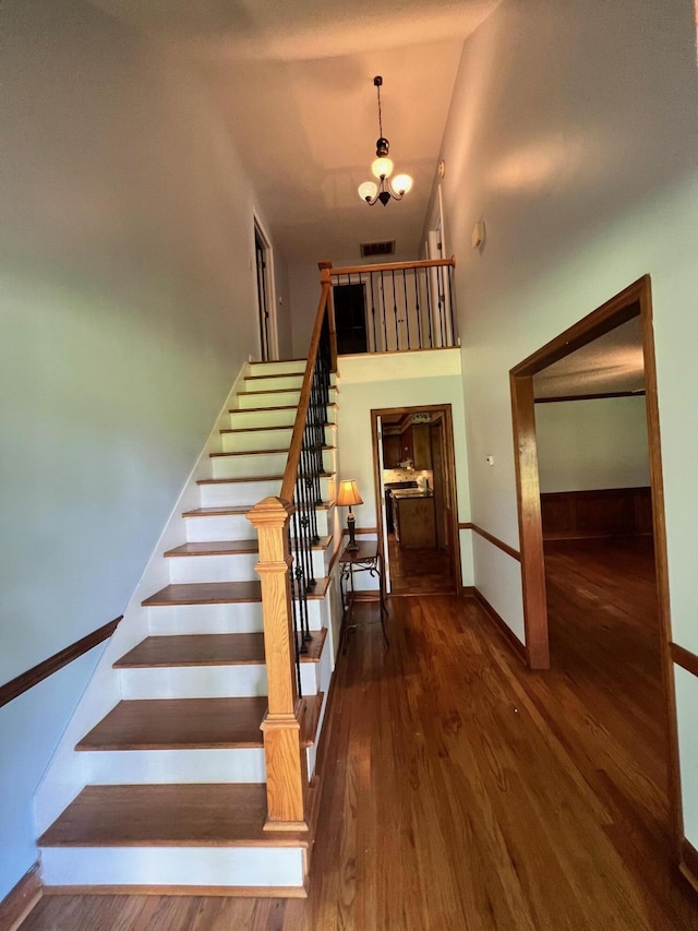 stairs featuring a towering ceiling, a notable chandelier, and hardwood / wood-style flooring