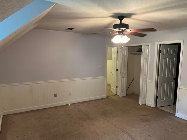 unfurnished bedroom featuring light carpet, a textured ceiling, lofted ceiling with skylight, ceiling fan, and a closet