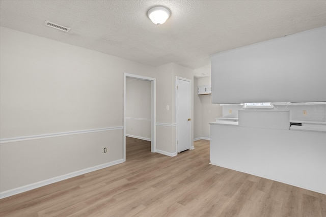empty room with light wood finished floors, visible vents, a textured ceiling, and baseboards