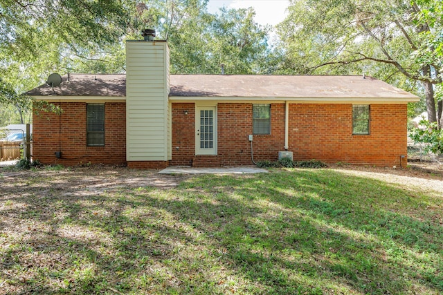 rear view of property featuring fence, a yard, brick siding, and a chimney