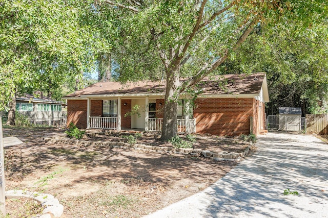 ranch-style home featuring brick siding, a porch, fence, and concrete driveway