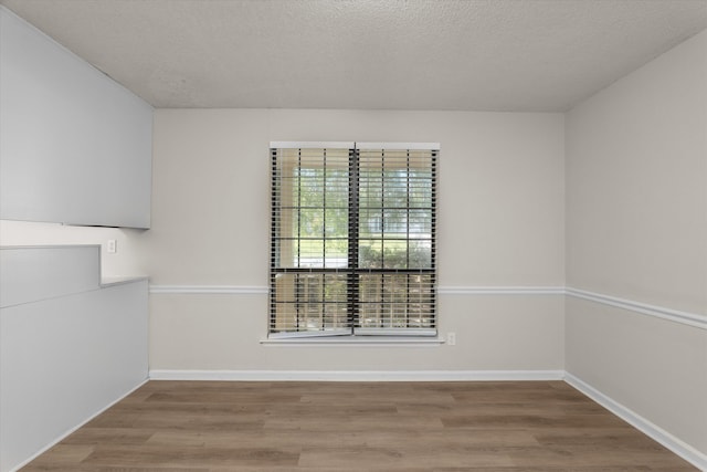 empty room with a textured ceiling, wood finished floors, and baseboards